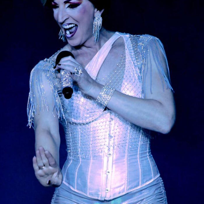 Fitta Drag con micrófono en el escenario durante un playback en La Cena de los Locos