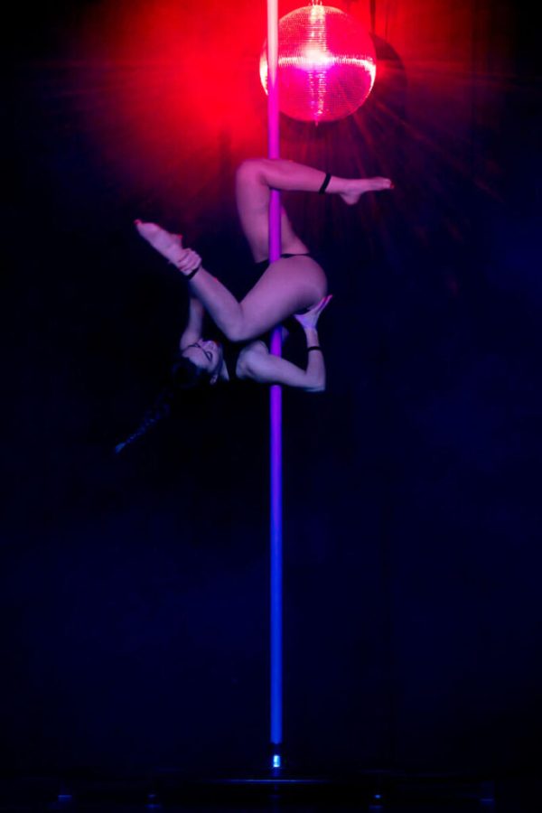 Fogg realizando una figura invertida de pole dance en el escenario de La Cena de los Locos